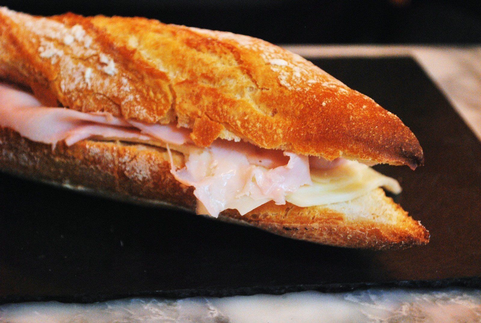 A sandwich with ham and cheese is sitting on a black plate.